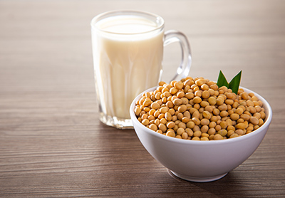 glass of soymilk next to a bowl of soybeans