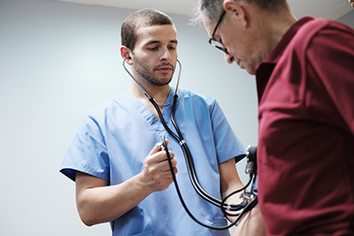 doctor checking older man's heart with a stethoscope.