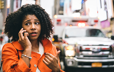 woman on the phone calling 911 with an abulance in the background