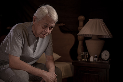 older man sitting at the side of the bed clearly upset that he cannot sleep