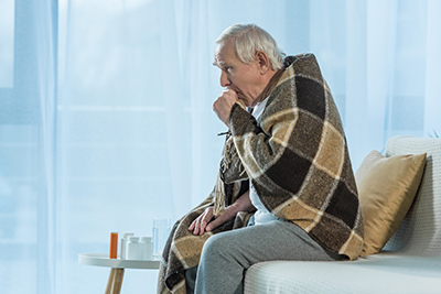 elderly man sitting on couch coughing