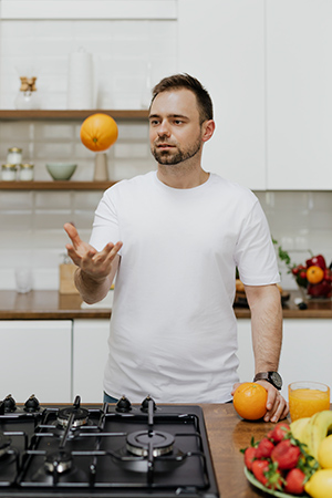 man throwing orange up in the air over a stove about to cook healthy