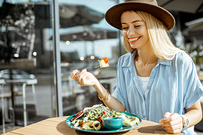 woman with hat on eating a plate of healthy food