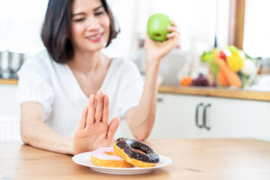 woman holding an apple in one hand and pushing away donuts on a plate