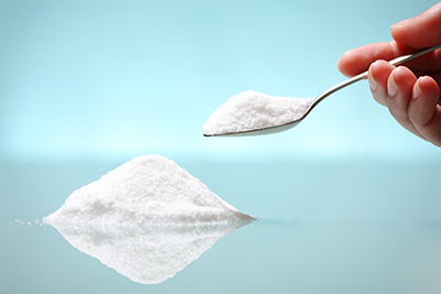 spoon being held full with sugar and sugar on the table