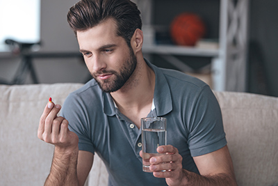 man holding a glass of water and a vitamin