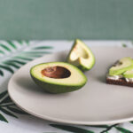 Avocado cut in half on a table with two slices on a sandwich