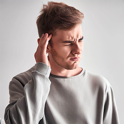 man suffering from the annoying sounds of tinnitus holding his hand to his head