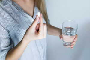 woman with glass of water in one hand and a pill in the other