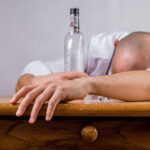 man slumped on a desk drunk and an empty liquor bottle in view
