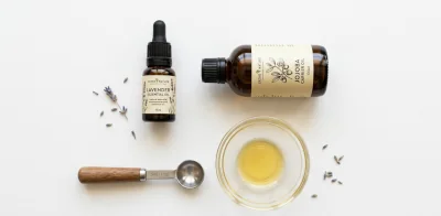Flat lay of a dark glass lavender essential oil bottle, a jojoba carrier oil bottle, a small glass mixing bowl all Essential oils for plantar fasciitis.