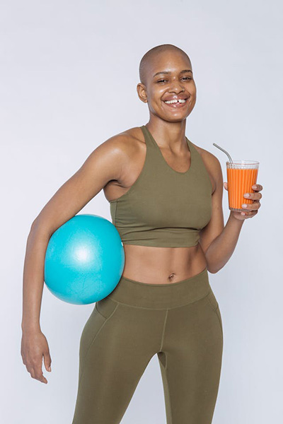 woman in workout clothes holding a glass of orange juice in one hand and a workout ball in the other
