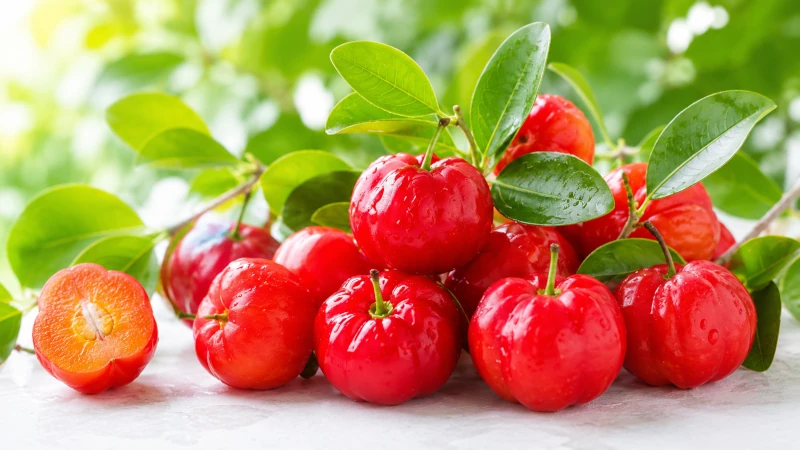 bright red acerola cherries with green leaves on a light fresh background.