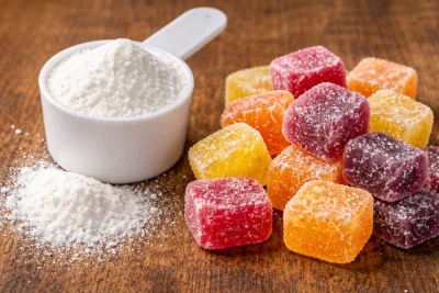 Creatine monohydrate powder in a scoop beside creatine gummies on a wooden surface.