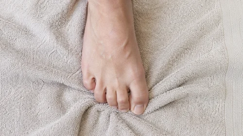 Bare foot curling toes on a white towel during a flat feet strengthening exercise.